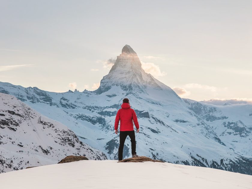 man wearing red puffer on sonwy mountain